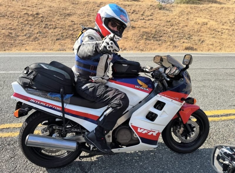 Rider in full gear on a white and red Honda VFR Interceptor sport bike giving a thumbs up on a California roadway